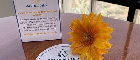 A table with a sign from Golden Mar Hotel, a flower, a placemat with the hotel's logo, and chocolate bars.
