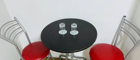 Uma mesa redonda pequena com duas cadeiras vermelhas, dois copos e um pano de mesa preto.
