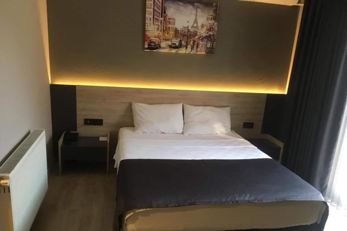 Quarto de hotel com uma cama grande, cabeceira com iluminação embutida, mesa de cabeceira e um quadro pendurado na parede.