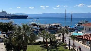 Vista costera con un barco grande en el puerto, un puerto deportivo con barcos y un aparcamiento con coches.