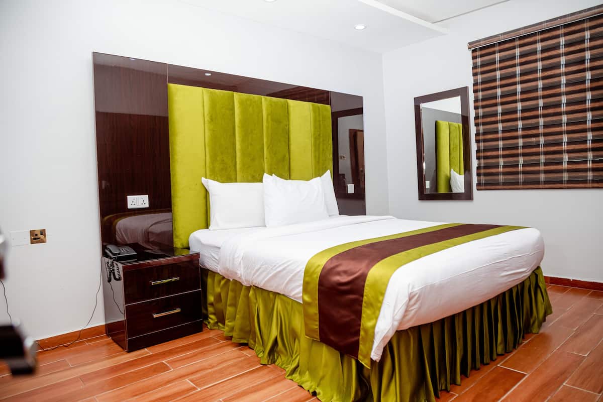 A hotel room with a large bed, a nightstand with a phone, and a mirror on the wall.