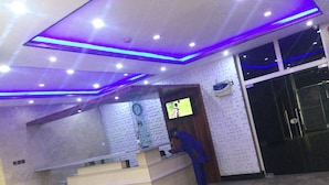 A reception area with a counter, a clock, and a TV screen displaying a sports event. - Novatel Hotel (Lekki)