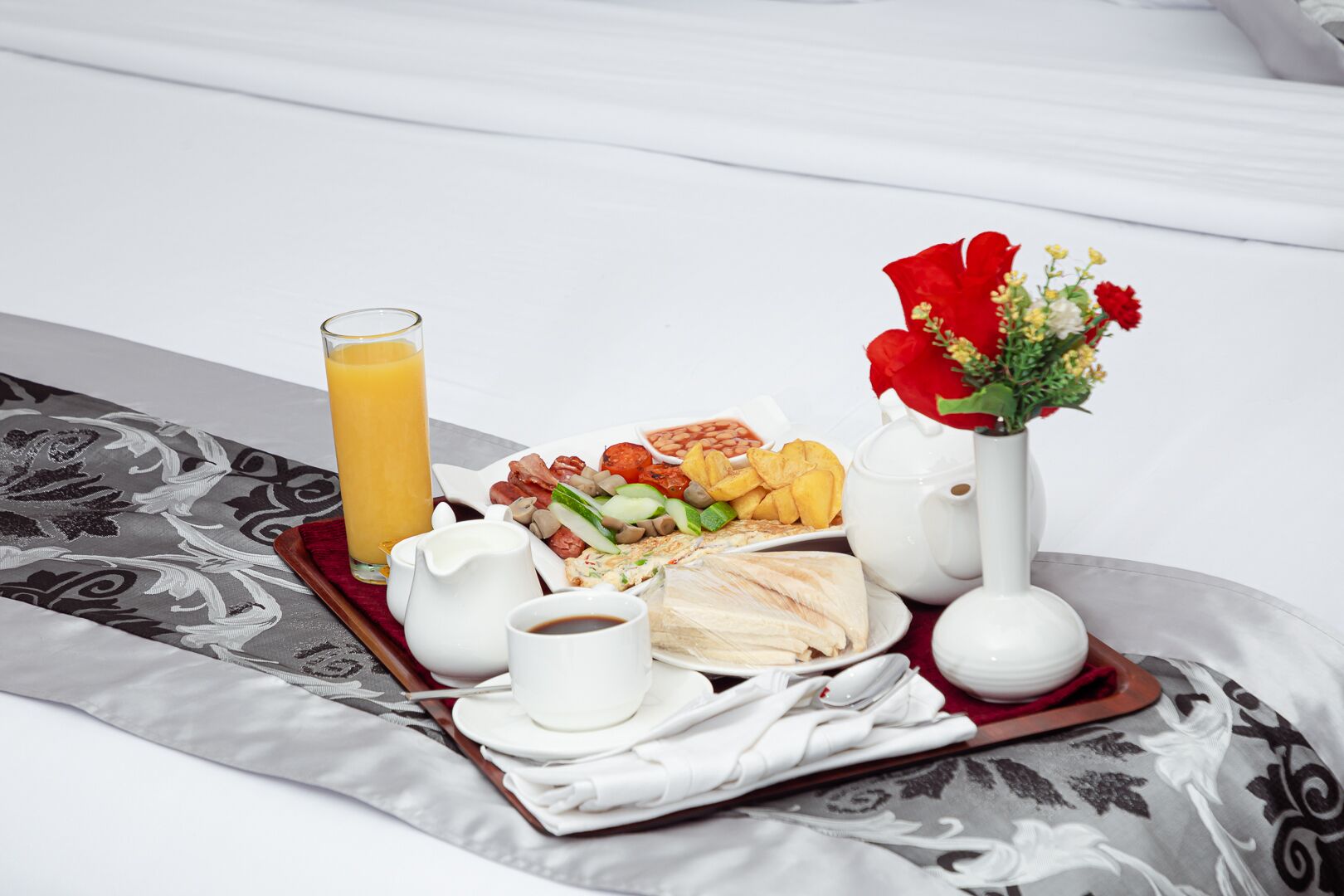 A breakfast tray with eggs, bacon, tomatoes, beans, and chips on a bed with a patterned bedspread.
