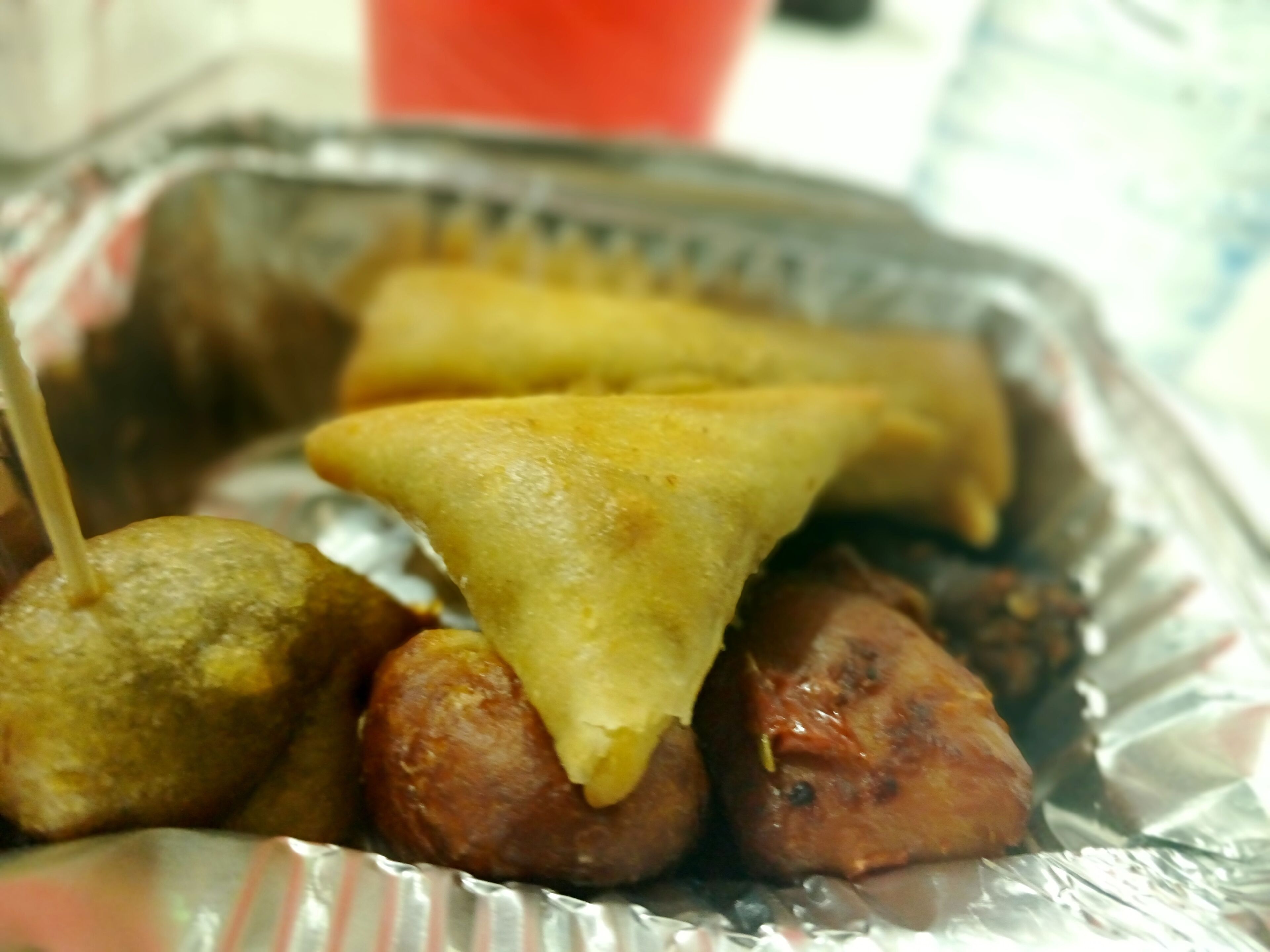 Una bandeja con diferentes comidas fritas, incluyendo samosas y salchichas.