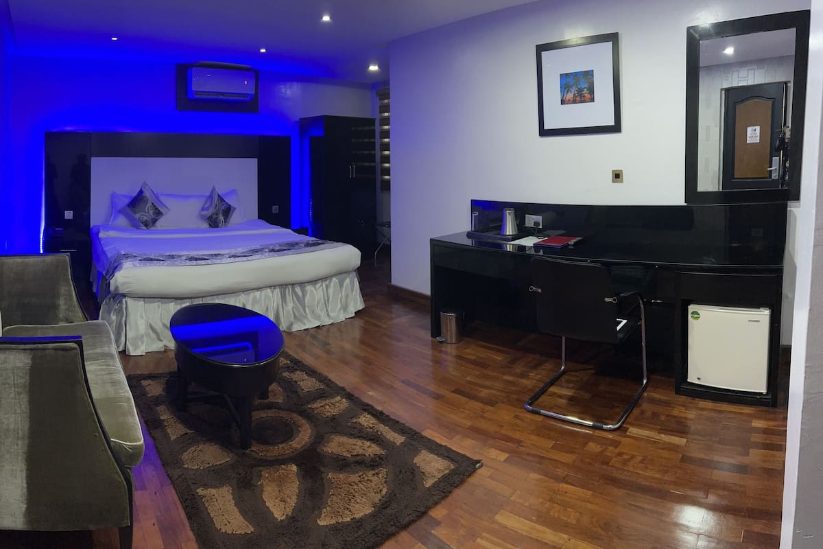 A bedroom with a bed, a desk, a chair, and a small refrigerator.
