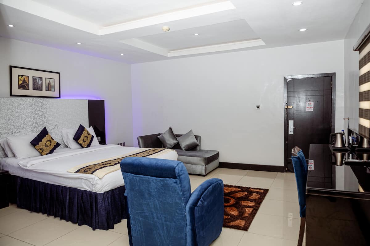 A modern bedroom with a large bed, a sofa, a desk, and a coffee machine.