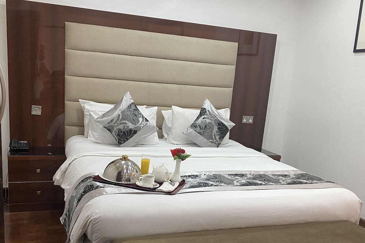 A neatly made bed with a headboard, a bedside table with a phone, and a tray with a cup, a glass of juice, and a flower.