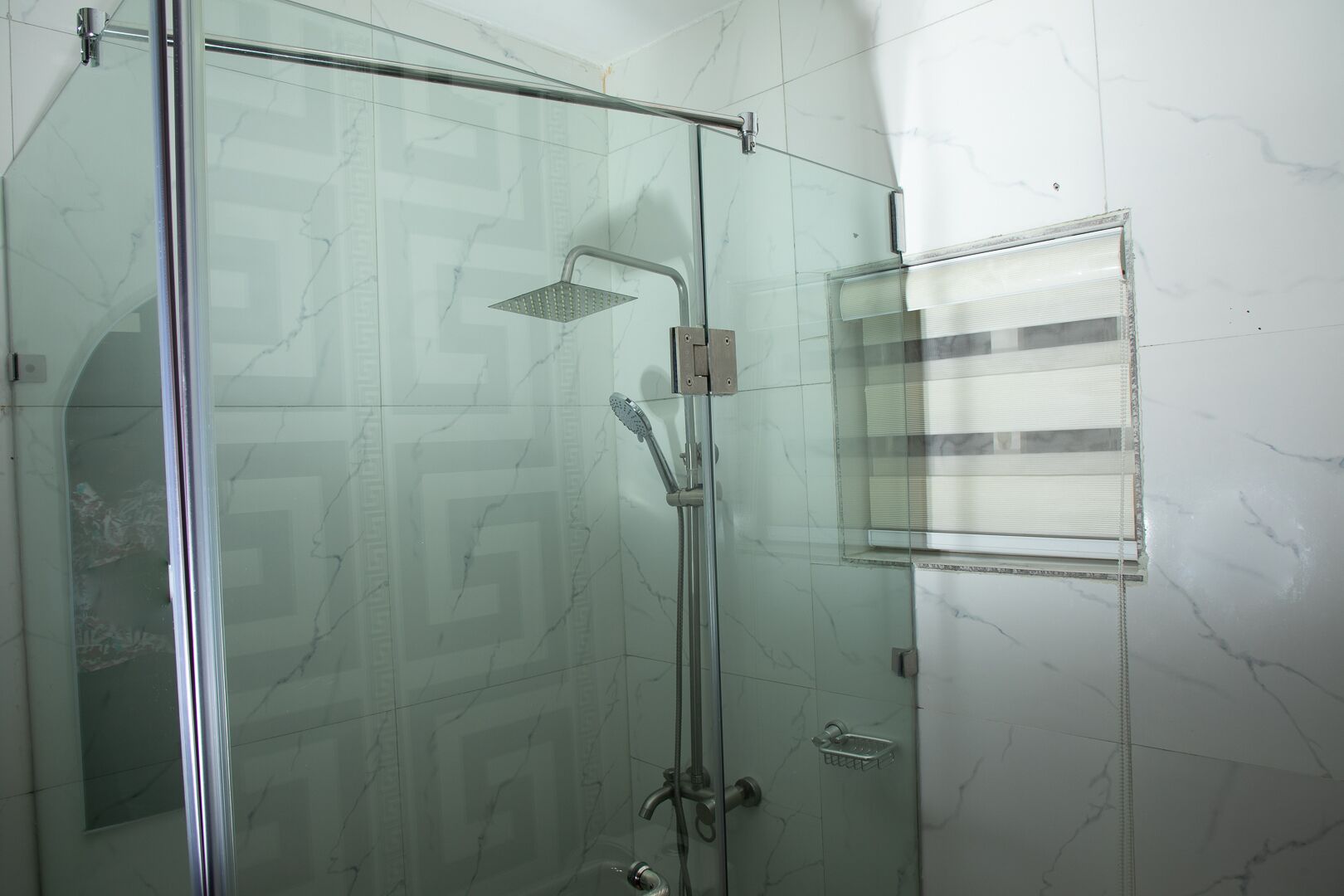A glass-enclosed shower with a handheld showerhead and a wall-mounted faucet.