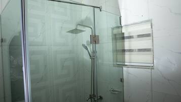A glass-enclosed shower with a handheld showerhead and a wall-mounted faucet.
