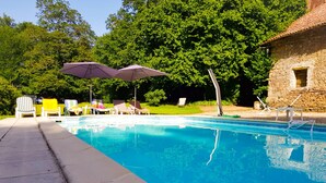 A swimming pool with lounge chairs and umbrellas, surrounded by greenery and a stone building. - Le château du Fraysseix à Roziers-Saint-Georges (Roziers-Saint-Georges)