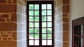 Une pièce d’angle avec un mur en pierre, une porte en bois et une fenêtre donnant sur un paysage verdoyant.