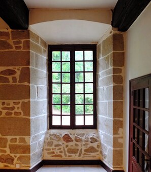 Une pièce d’angle avec un mur en pierre, une porte en bois et une fenêtre donnant sur un paysage verdoyant.