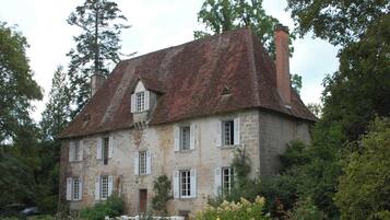 Un bâtiment en pierre doté de nombreuses fenêtres et d’un toit rouge, entouré de verdure.
