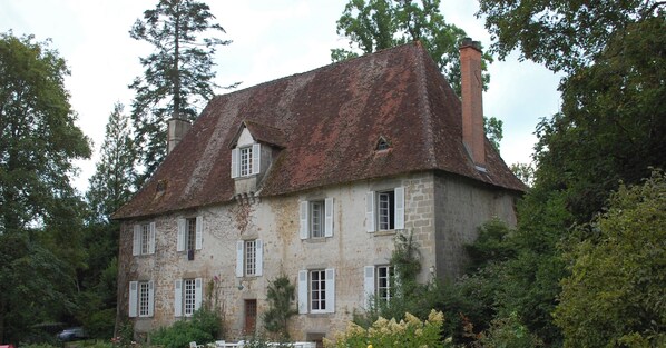 Un bâtiment en pierre doté de nombreuses fenêtres et d’un toit rouge, entouré de verdure.