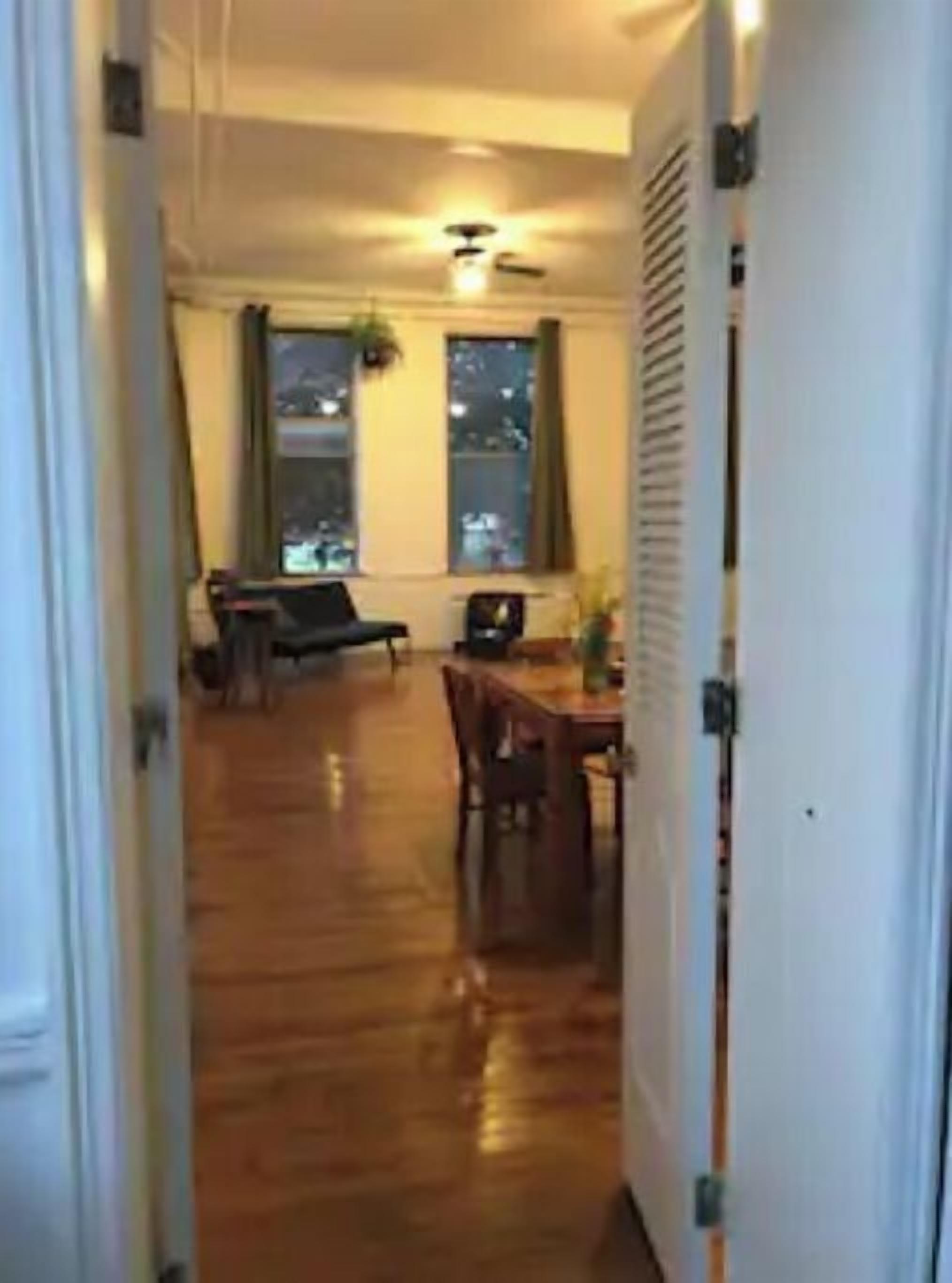 A hallway leading to a dining area with a wooden floor, a dining table, chairs, and a ceiling fan.