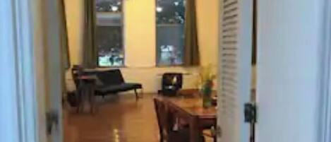 A hallway leading to a dining area with a wooden floor, a dining table, chairs, and a ceiling fan.