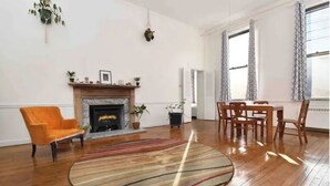 A spacious living room with a fireplace, wooden flooring, a round rug, and a dining area with chairs. - Creative living 4 (Youngstown)
