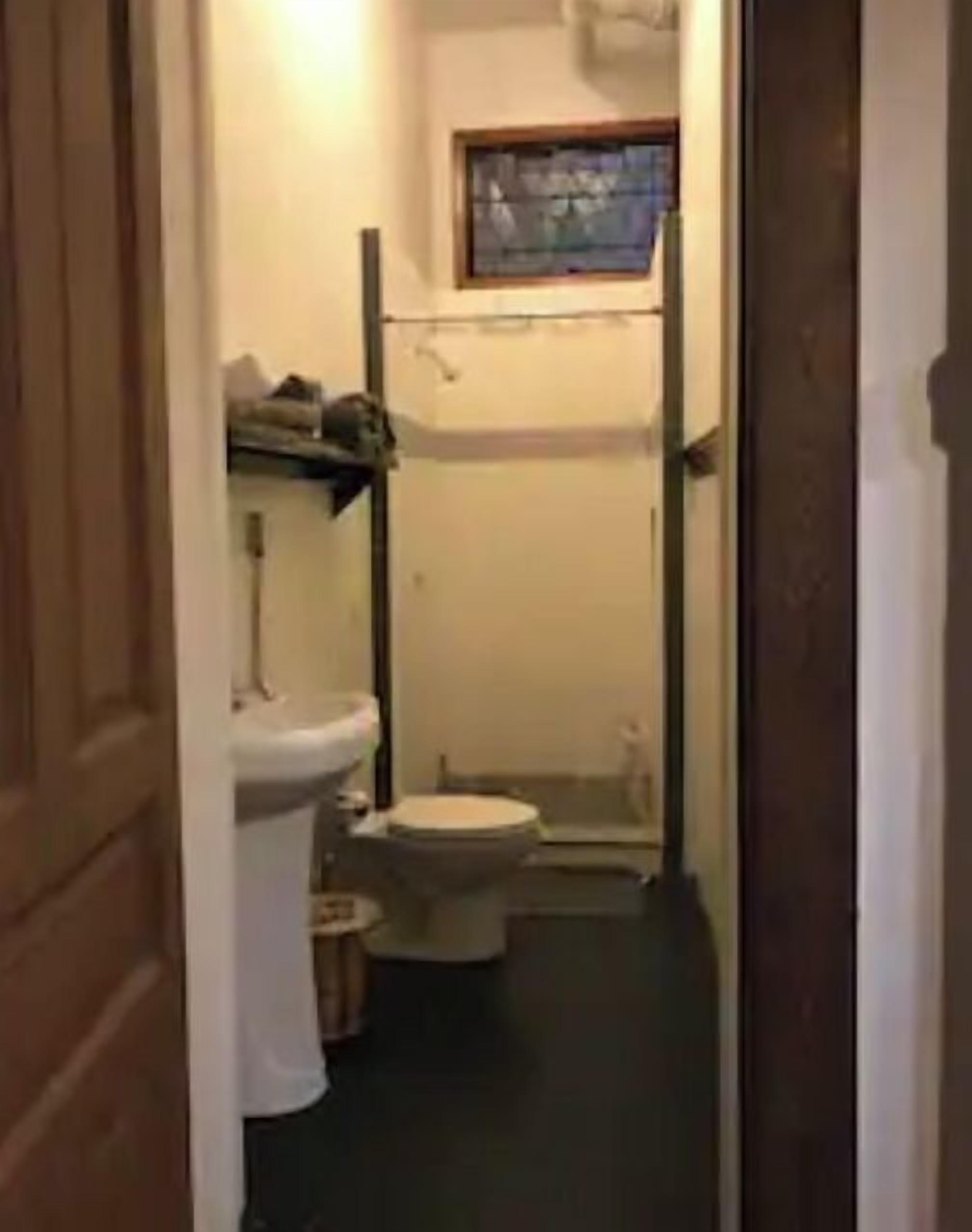 Un couloir étroit mène à une salle de bain équipée de toilettes, d’une douche et d’une petite fenêtre.