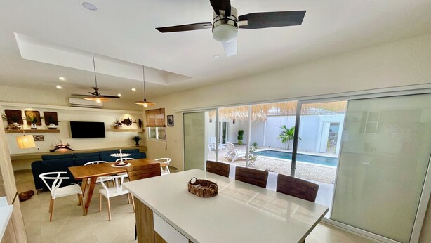 A modern kitchen with a central island, dining area, and a view of a swimming pool. - Amazing new modern house close to the beach (Potrero)