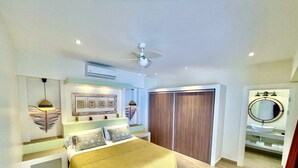 A bedroom with a bed, bedside tables, a ceiling fan, a wardrobe, and a bathroom with a sink and mirror. - Amazing new modern house close to the beach (Potrero)