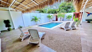 A pool area with lounge chairs, a thatched roof, and a small pool. - Amazing new modern house close to the beach (Potrero)