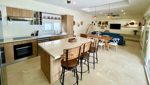 A modern kitchen with a central island, bar stools, and a dining area with a blue sofa. - Amazing new modern house close to the beach (Potrero)