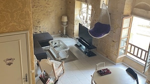 A rustic room with a stone wall, a hanging chair, a sofa, a TV, and a dining table with chairs.