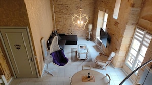 A spacious living area with a high ceiling, a hanging chair, a round dining table, and a fireplace.