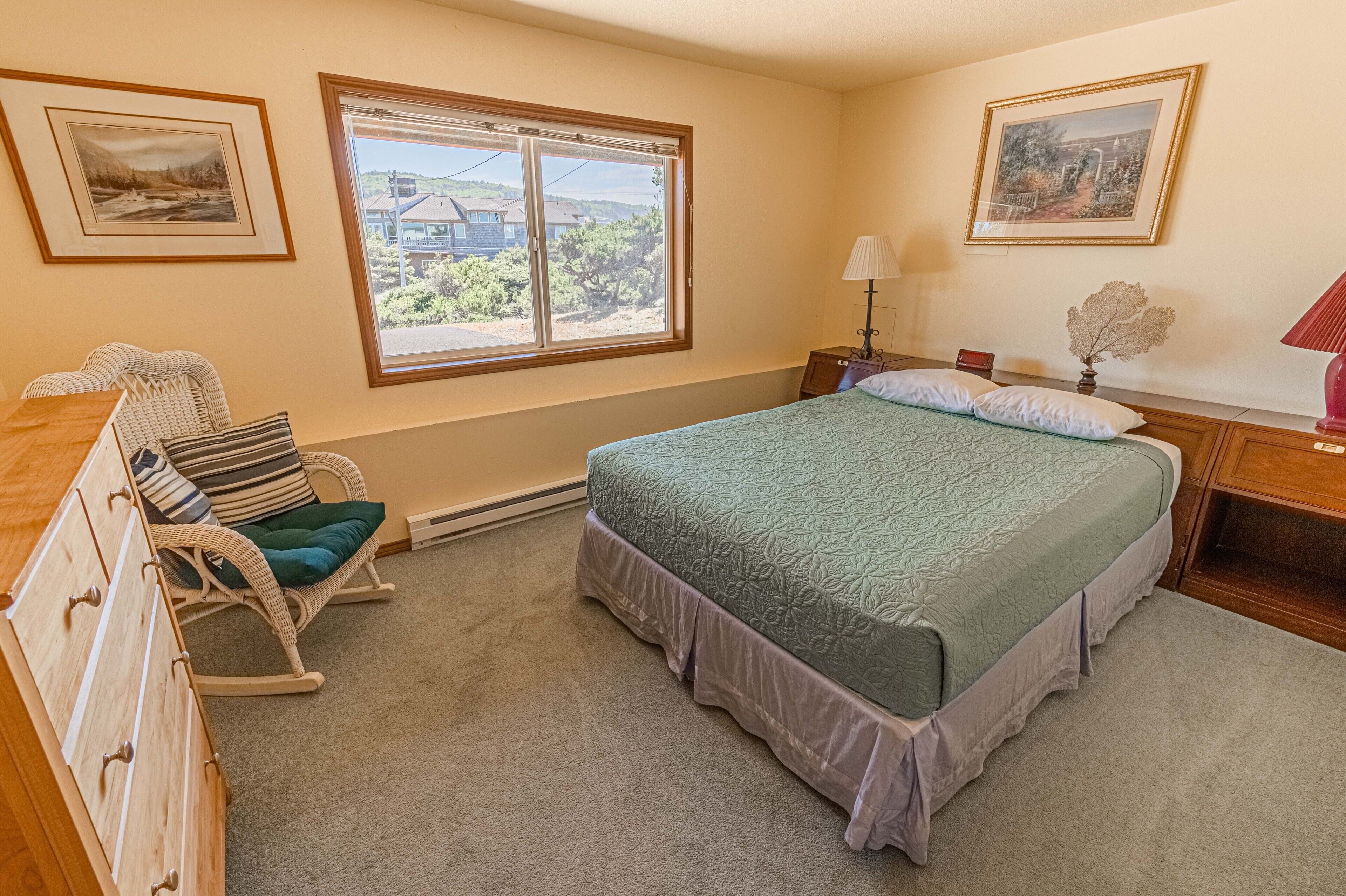 A bedroom with a bed, a rocking chair, a dresser, a nightstand, a lamp, and two framed pictures on the wall.