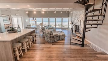A spacious living area with a large window overlooking the beach, a cozy seating area, and a modern staircase.