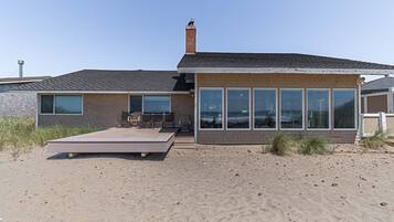 A modern beach house with a large deck, a brick exterior, and large windows.