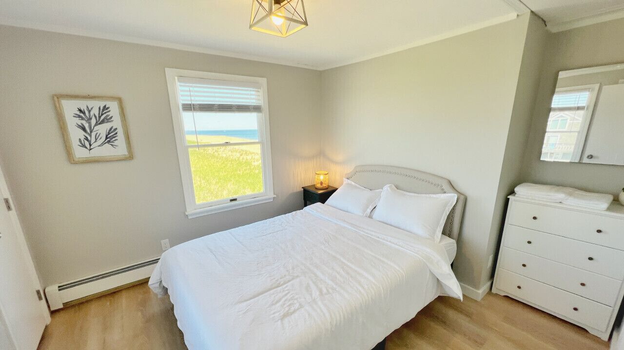 Un dormitorio con cama, mesita de noche, cómoda, ventana con vistas y espejo en la pared.