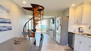 Een moderne keuken met een spiltrap, een eethoek met een houten tafel en stoelen, en uitzicht op de oceaan door het raam.