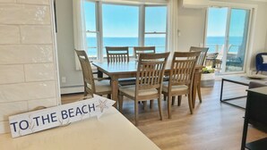 Un coin repas avec vue sur la mer, un panneau indiquant « VERS LA PLAGE », et un balcon avec une chaise.