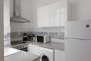 A kitchen with white cabinets, a microwave, a toaster, a stove, and a washing machine. - Tribuna - San Telmo Boutique Apartment (Málaga)