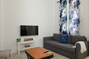 A living room with a flat-screen TV, a grey sofa, a wooden coffee table, and a white side table with books. - Tribuna - San Telmo Boutique Apartment (Málaga)