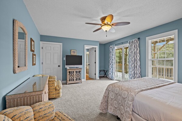A bedroom with a bed, a television, a ceiling fan, and a view of the outdoors through a door. - Duplex with private pool and easy beach access,in the Spinnaker's Reach (Emerald Isle)