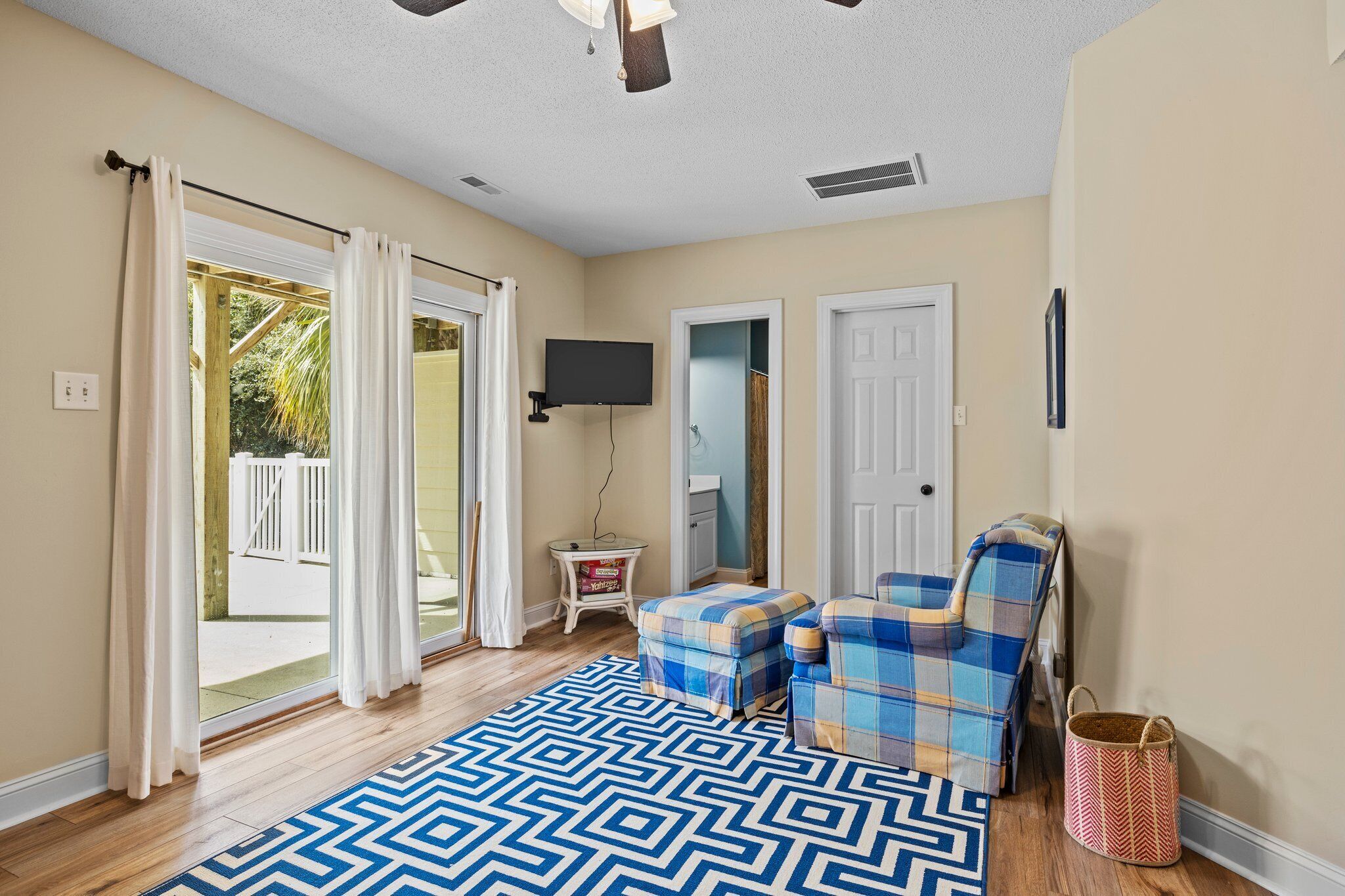 A room with a patterned rug, a plaid armchair, a small table, and a television mounted on the wall.