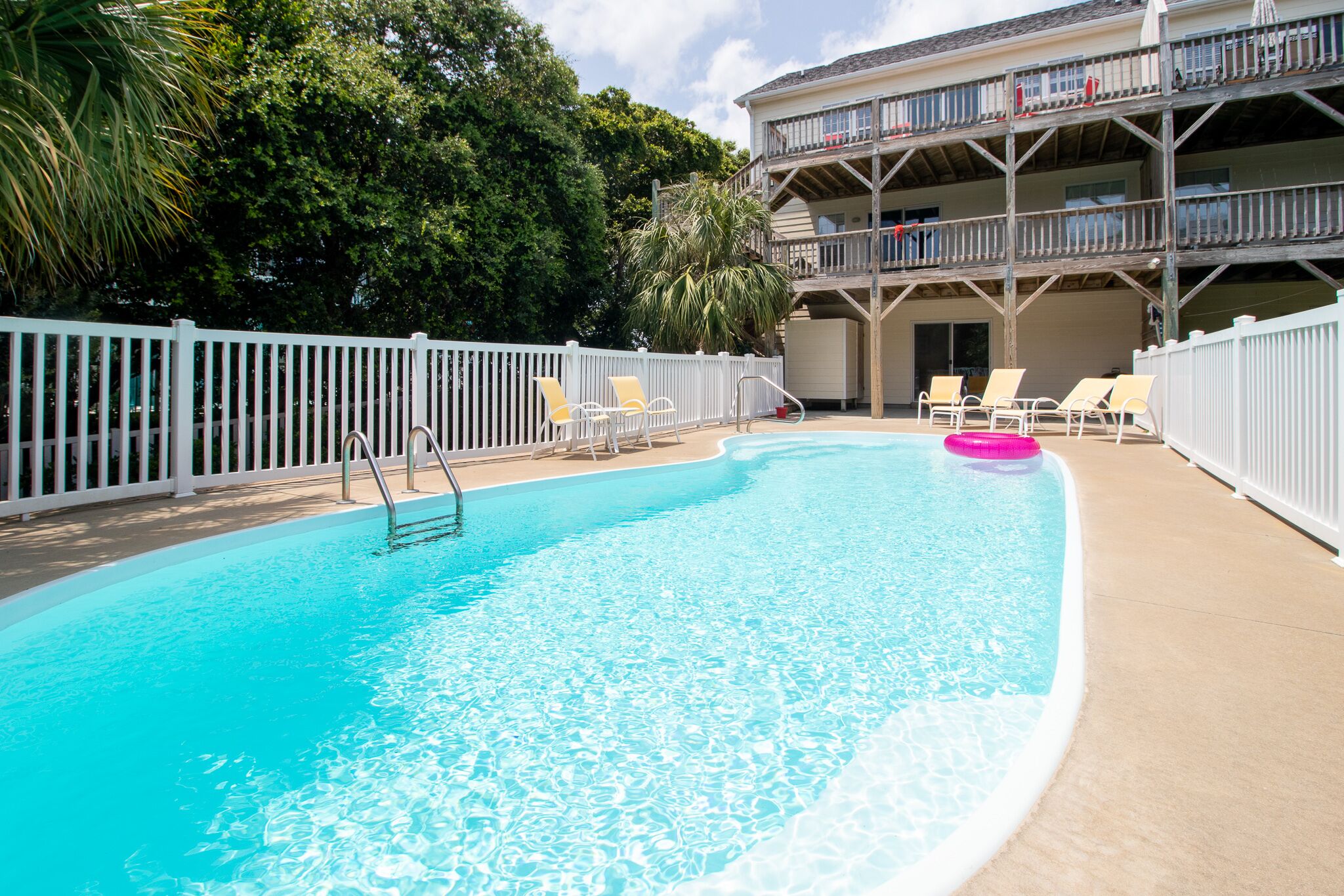 A swimming pool with lounge chairs and a white fence.