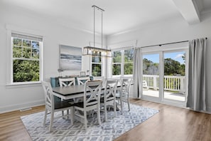 Un espace repas comprenant une table et des chaises, un luminaire suspendu et de grandes fenêtres donnant sur un paysage verdoyant.