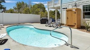 A swimming pool with a metal ladder, lounge chairs, and a wooden deck area.