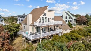 A two-story house with a balcony and a deck, surrounded by trees and other houses.