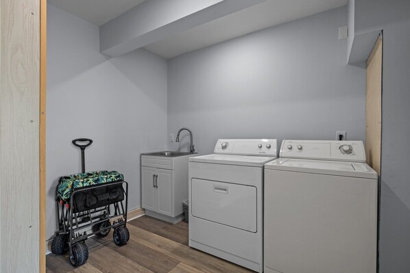 A laundry room with a washing machine, dryer, sink, and a stroller.