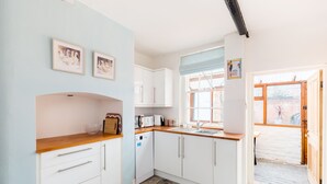 A modern kitchen with white cabinets, a wooden countertop, and a stone floor. There are framed pictures on the wall, and a window with a view of the outside. - Shakespeare House, Free Parking, Town Centre Location (Stratford-upon-Avon)