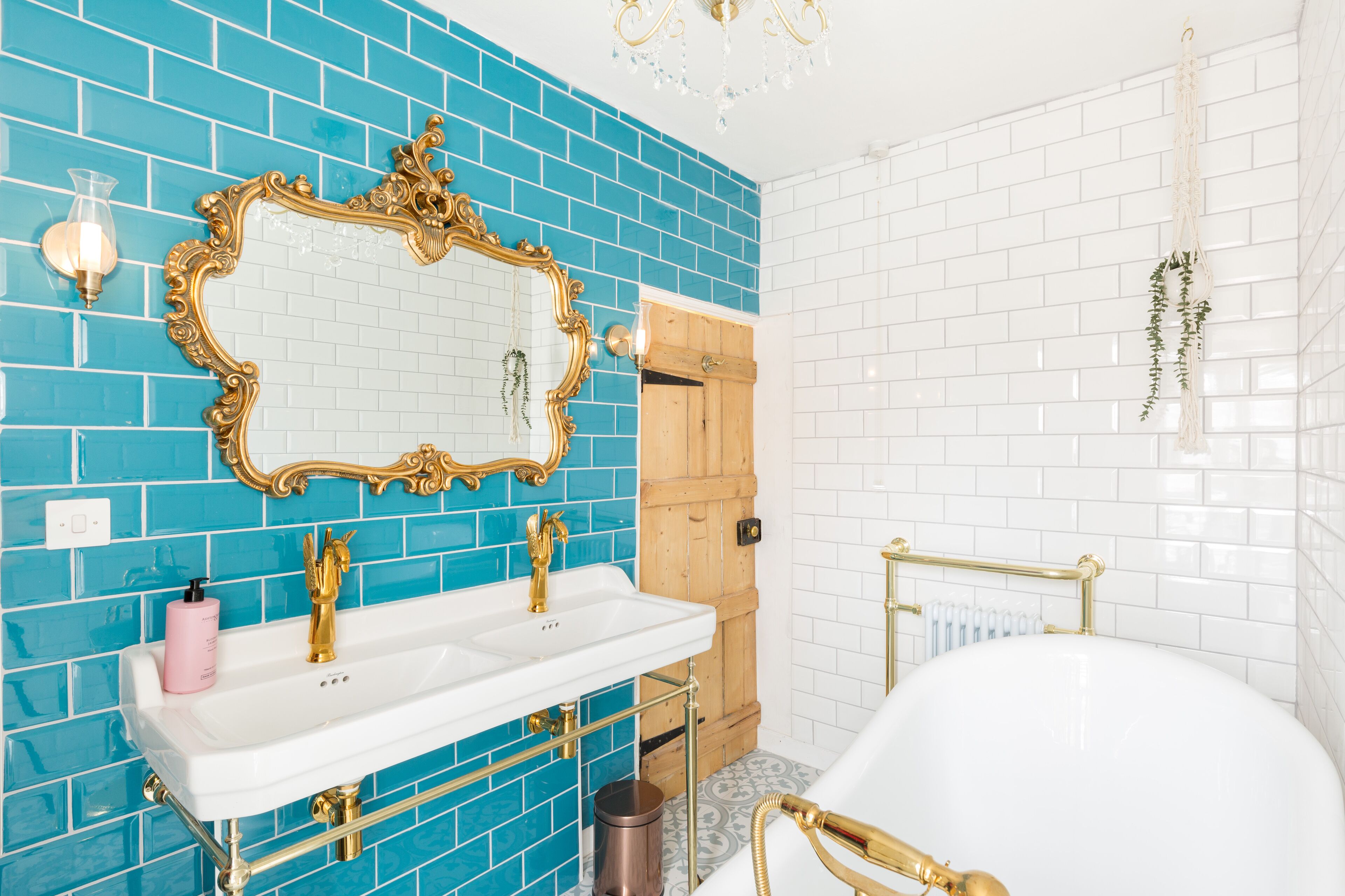 A bathroom with a white sink, gold fixtures, a large mirror, and blue-tiled walls.
