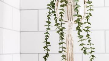A macrame hanging planter with green foliage against a white tiled wall.