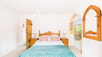 A bedroom with a wooden bed, two bedside tables with lamps, a wooden wardrobe, a wall-mounted mirror, and a floral artwork.