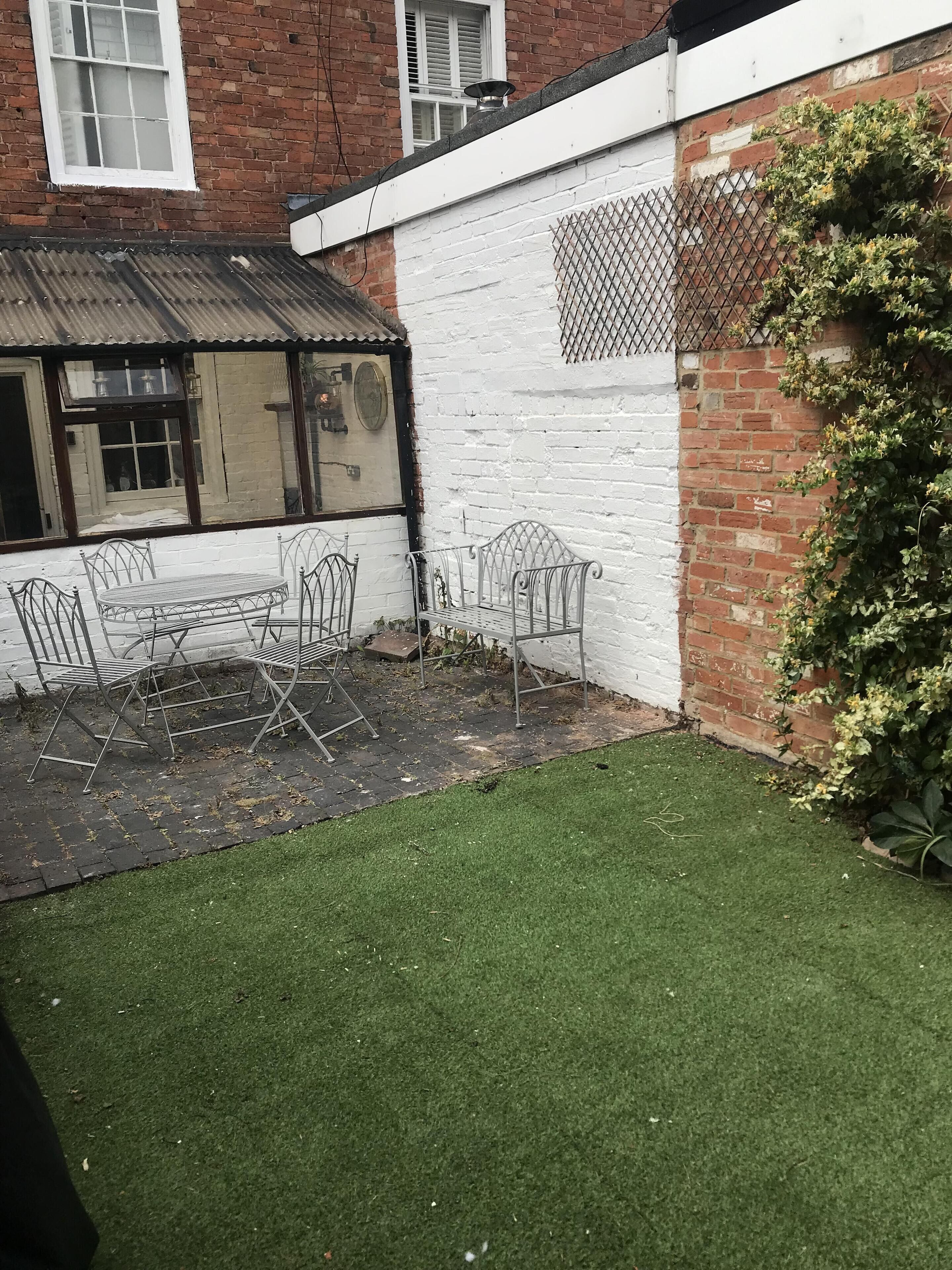A courtyard with a metal table and chairs, a white brick wall, and a green lawn.