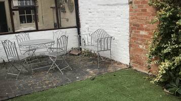 A courtyard with a metal table and chairs, a white brick wall, and a green lawn.