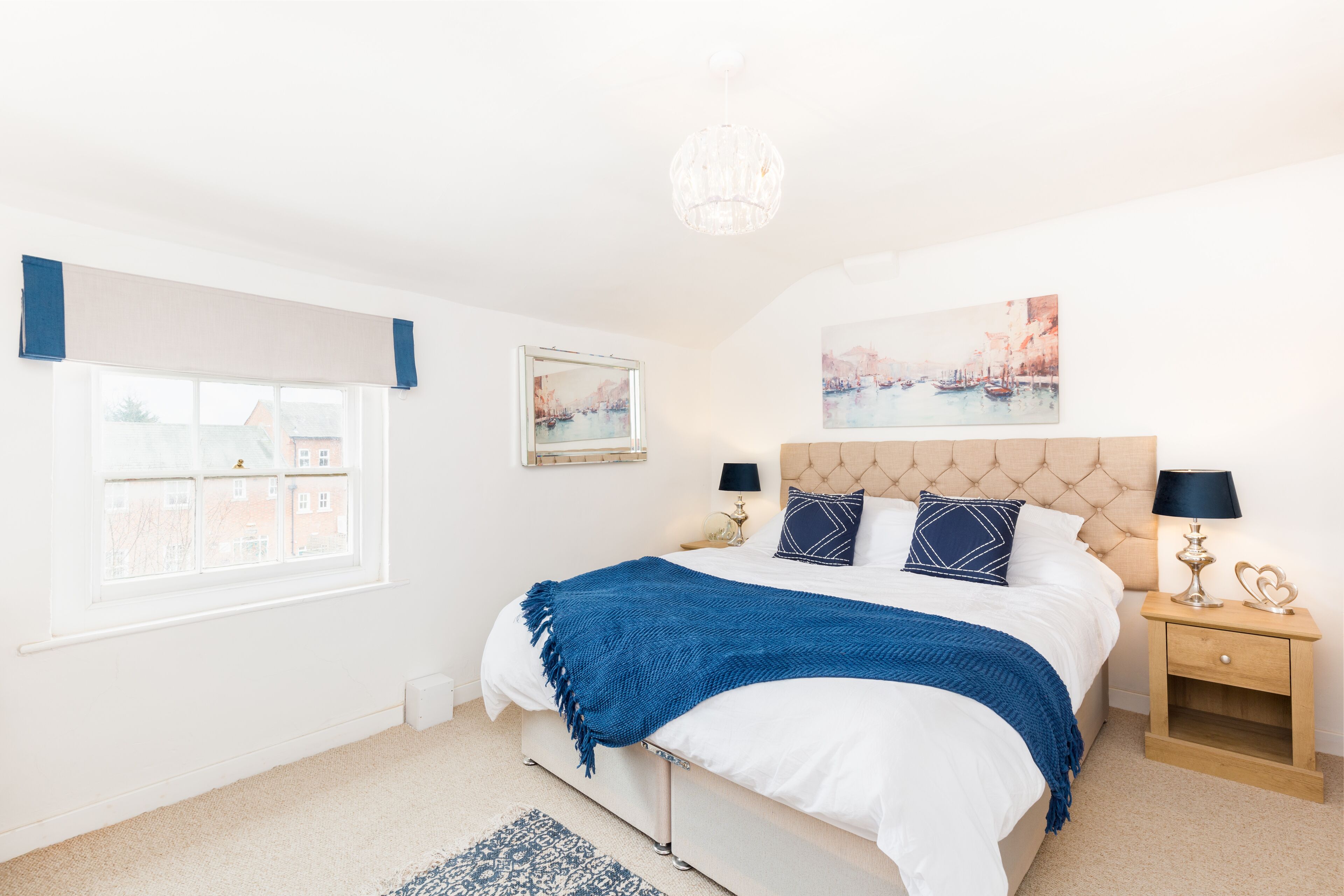 A bedroom with a bed, bedside tables, a chandelier, and artwork on the walls.